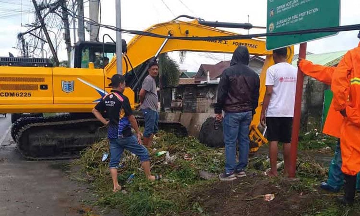 Workers use an excavator to clear debris from Amuco Creek in Magalang while rain continues to fall.