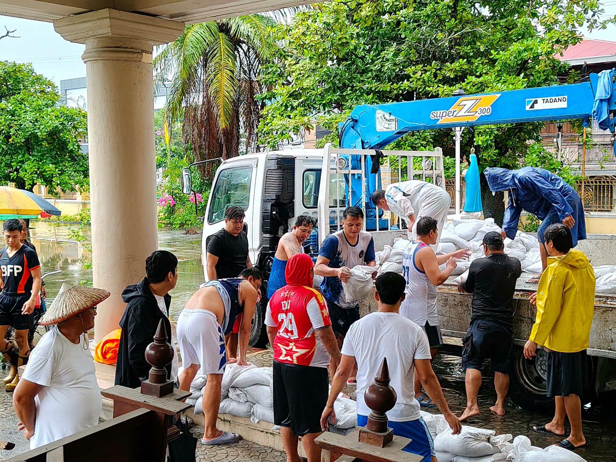 Residents and responders unload sandbags beside floodwater at Santa Rita de Cascia Parish Church.